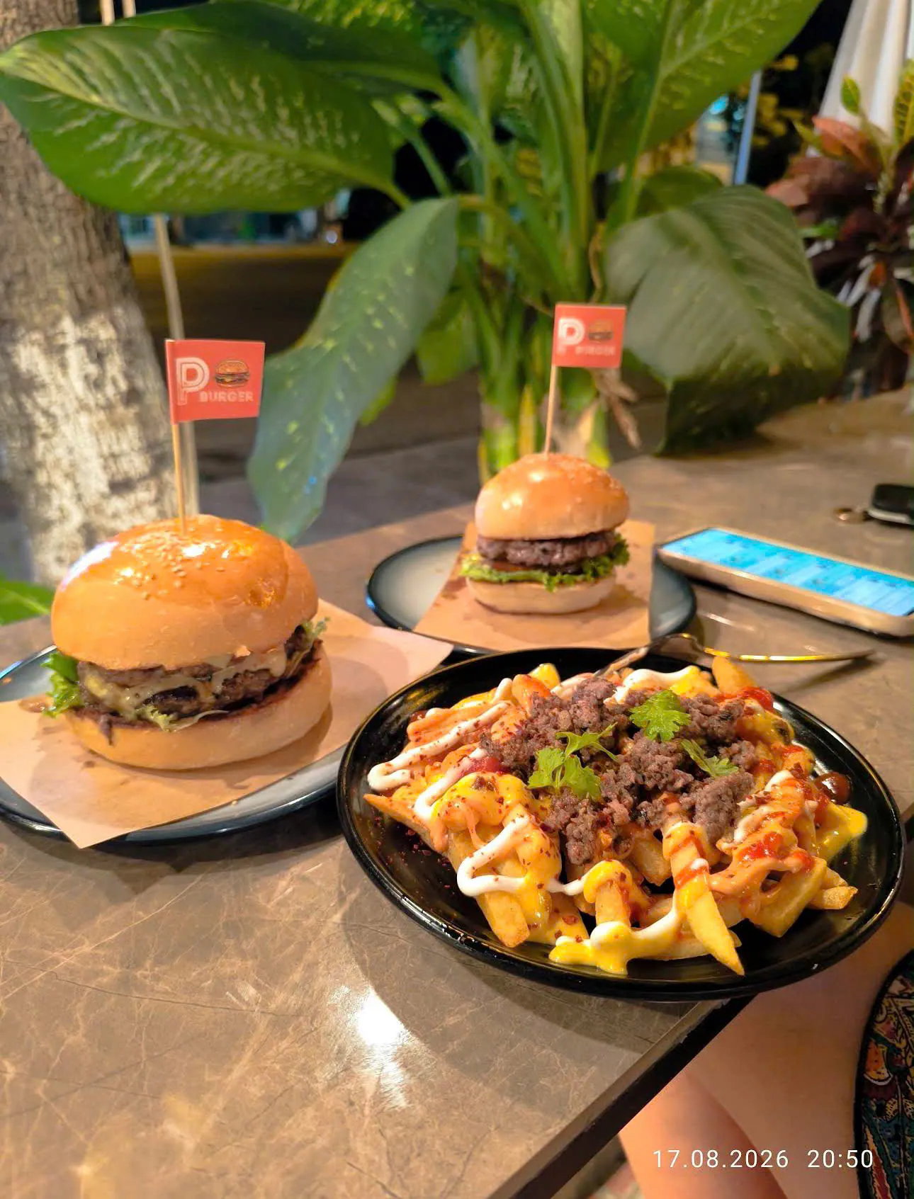 Burgers and loaded fries on a table under the plants at night